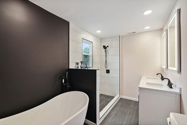 full bathroom featuring visible vents, a freestanding bath, vanity, tiled shower, and baseboards