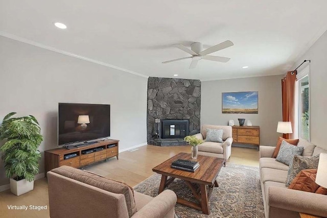 living room featuring crown molding, a stone fireplace, light wood finished floors, and ceiling fan