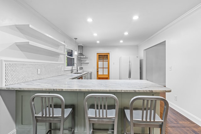 kitchen featuring sink, white refrigerator, kitchen peninsula, crown molding, and wall chimney exhaust hood