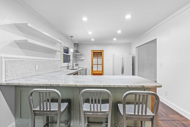 kitchen with open shelves, freestanding refrigerator, a sink, wall chimney range hood, and a peninsula