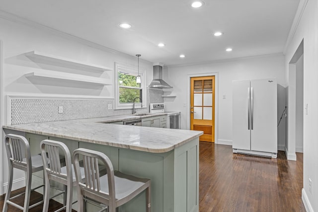 kitchen featuring a peninsula, white appliances, wall chimney range hood, open shelves, and pendant lighting