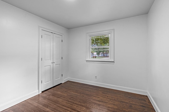 unfurnished bedroom with dark wood-style floors, a closet, and baseboards