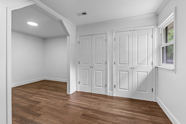 unfurnished bedroom featuring arched walkways, dark wood-type flooring, visible vents, two closets, and crown molding