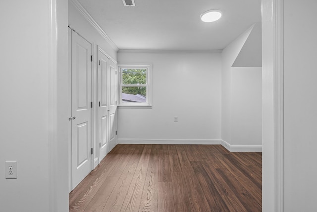 unfurnished bedroom featuring visible vents, multiple closets, baseboards, dark wood finished floors, and crown molding