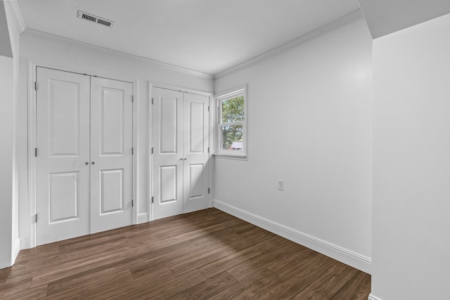 unfurnished bedroom featuring dark wood-type flooring, ornamental molding, and multiple closets