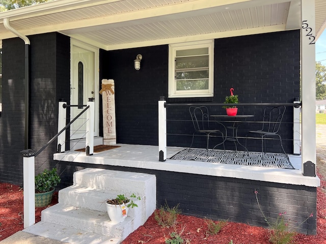 property entrance featuring covered porch and brick siding