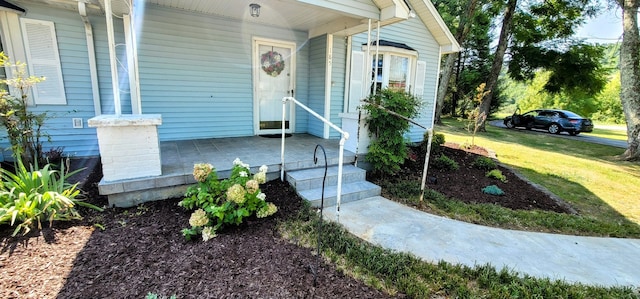 view of exterior entry featuring a porch and a lawn