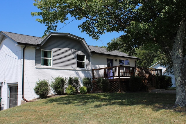 back of house with roof with shingles, an attached garage, a deck, a yard, and brick siding