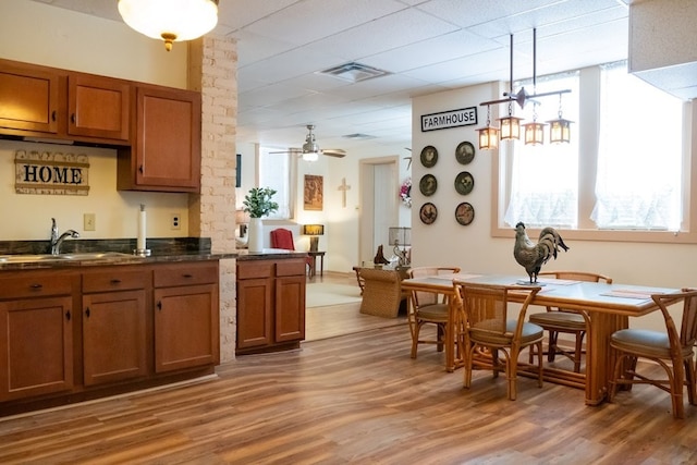 kitchen with wood-type flooring, ceiling fan, pendant lighting, brick wall, and sink