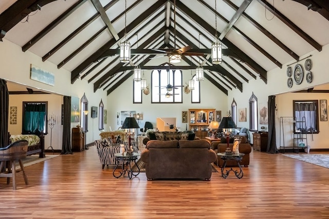 living room featuring beam ceiling, ceiling fan with notable chandelier, wood-type flooring, and high vaulted ceiling