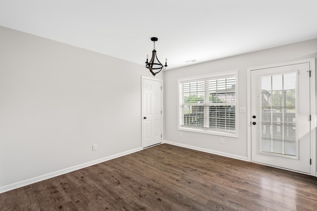 unfurnished dining area with dark wood-type flooring, a chandelier, and a wealth of natural light