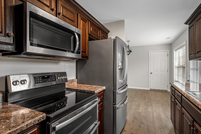 kitchen featuring dark stone countertops, light hardwood / wood-style flooring, appliances with stainless steel finishes, and dark brown cabinetry