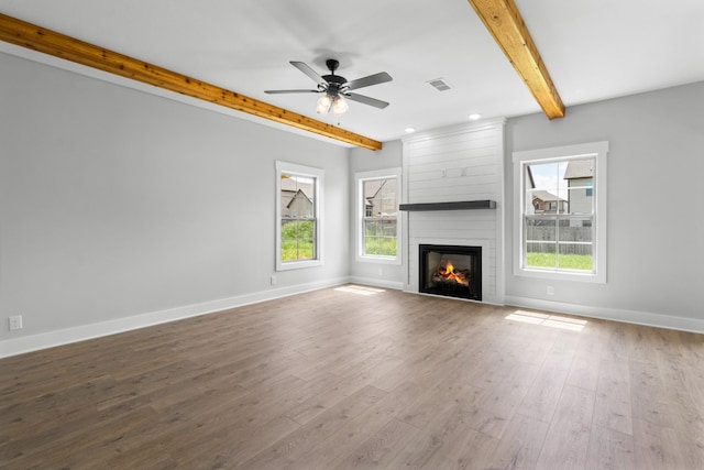 unfurnished living room featuring hardwood / wood-style floors, beam ceiling, a large fireplace, and ceiling fan