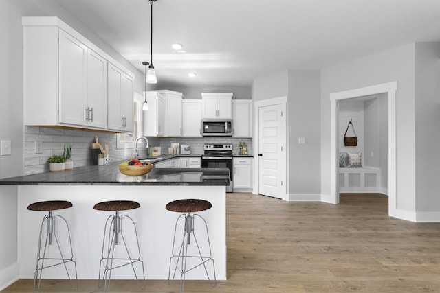 kitchen featuring stainless steel appliances, a breakfast bar, white cabinets, and decorative light fixtures