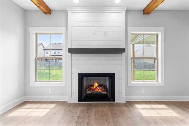 unfurnished living room with a large fireplace, beamed ceiling, and light hardwood / wood-style floors