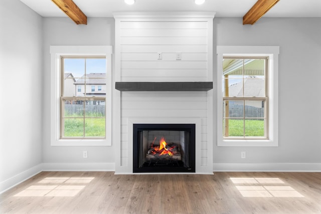 unfurnished living room with beam ceiling, a fireplace, a wealth of natural light, and light wood-type flooring