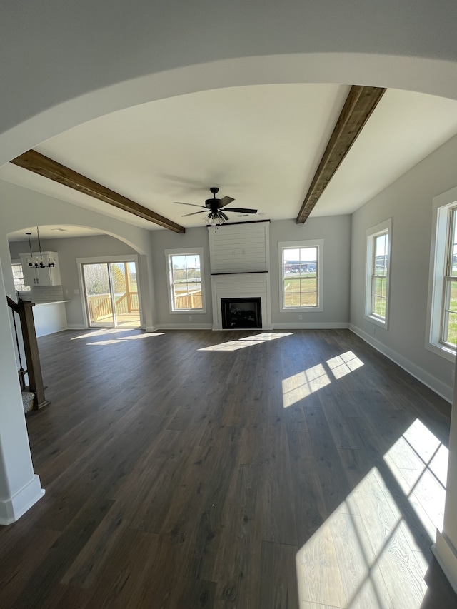 unfurnished living room featuring beamed ceiling, dark wood-type flooring, ceiling fan with notable chandelier, and a fireplace