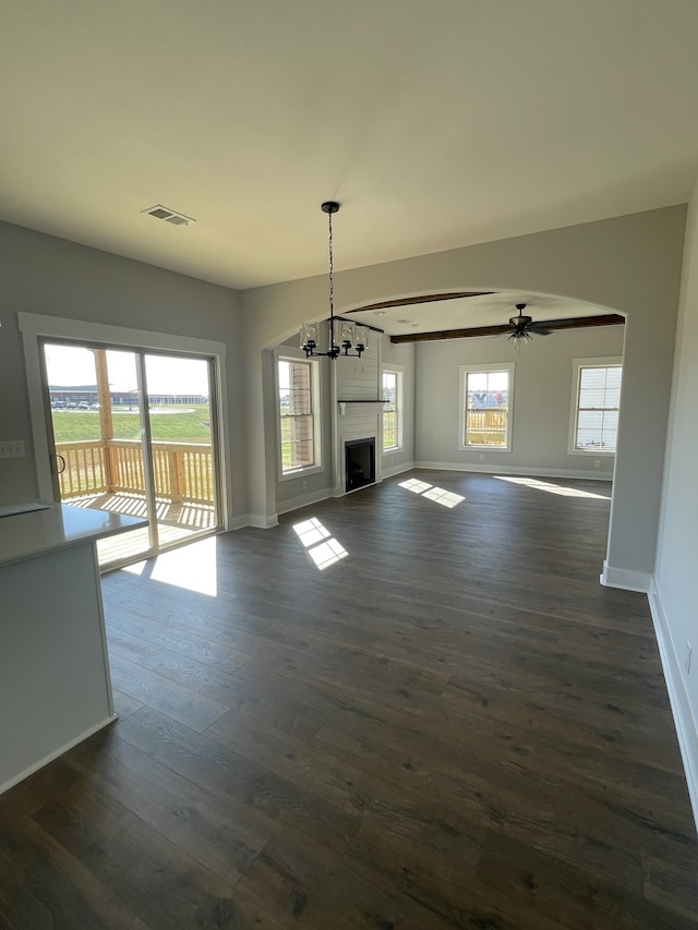 unfurnished living room featuring dark wood-type flooring, a wealth of natural light, and ceiling fan with notable chandelier