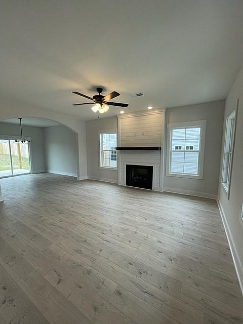 unfurnished living room featuring ceiling fan, a large fireplace, light wood-type flooring, and a wealth of natural light