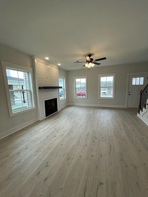 unfurnished living room with ceiling fan, a fireplace, and light hardwood / wood-style flooring