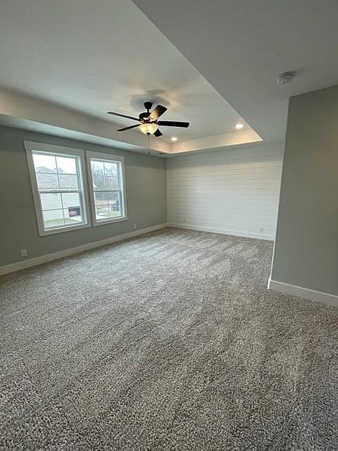 carpeted spare room with a tray ceiling and ceiling fan