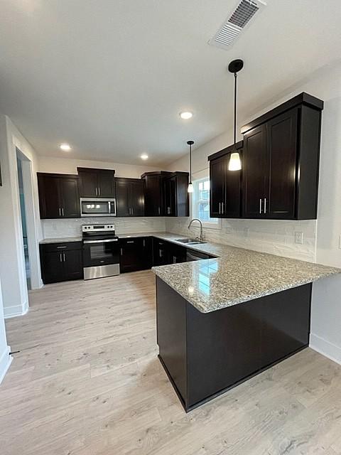 kitchen with appliances with stainless steel finishes, pendant lighting, sink, kitchen peninsula, and light wood-type flooring