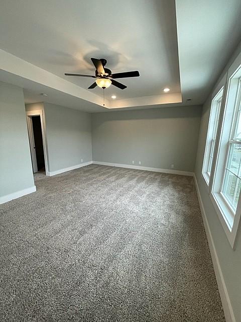 carpeted empty room with a raised ceiling and ceiling fan