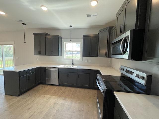 kitchen with appliances with stainless steel finishes, sink, hanging light fixtures, kitchen peninsula, and light hardwood / wood-style flooring