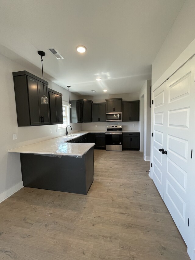 kitchen with sink, hanging light fixtures, stainless steel appliances, light hardwood / wood-style floors, and kitchen peninsula