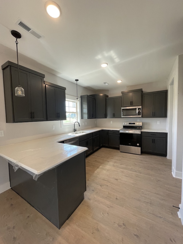 kitchen featuring sink, light hardwood / wood-style flooring, appliances with stainless steel finishes, decorative light fixtures, and kitchen peninsula