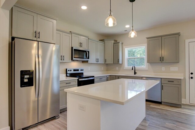 kitchen with appliances with stainless steel finishes, a kitchen island, sink, and light wood-type flooring