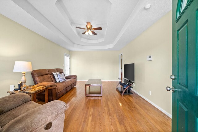 living room featuring wood-type flooring, ceiling fan, and a tray ceiling