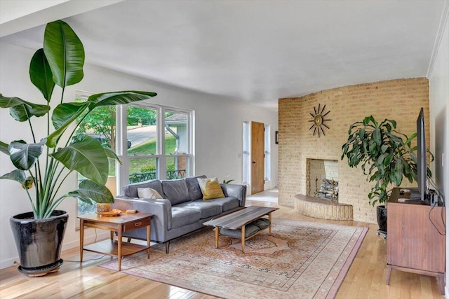 living room with brick wall, a fireplace, light hardwood / wood-style flooring, and ornamental molding