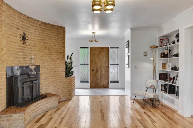 foyer with brick wall, ornamental molding, an inviting chandelier, and light wood-type flooring