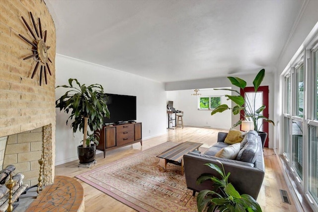 living room with a brick fireplace, brick wall, light wood-type flooring, and ceiling fan