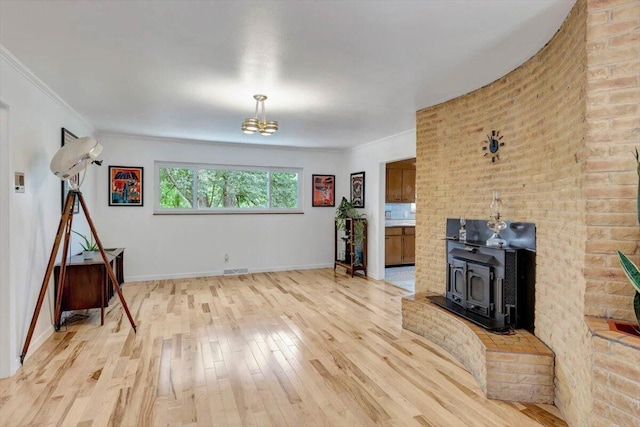 living room with brick wall, crown molding, light hardwood / wood-style floors, and a wood stove