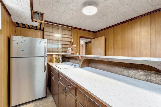 kitchen with sink, crown molding, wood walls, and stainless steel refrigerator