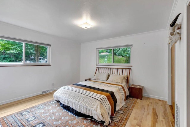 bedroom featuring multiple windows, crown molding, and light wood-type flooring