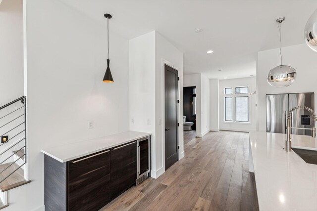 kitchen featuring wine cooler, stainless steel fridge with ice dispenser, dark brown cabinets, pendant lighting, and hardwood / wood-style floors