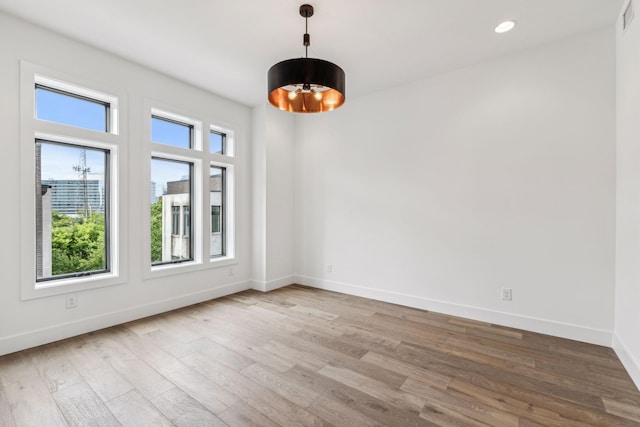 empty room featuring a notable chandelier and light wood-type flooring