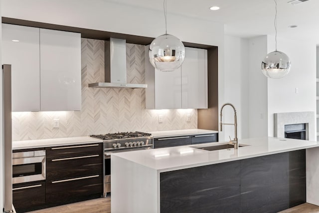 kitchen with pendant lighting, sink, gas stove, white cabinets, and wall chimney exhaust hood