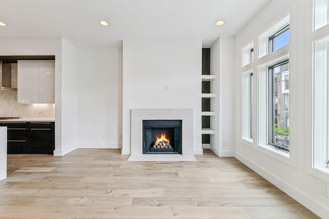 unfurnished living room featuring built in features and light hardwood / wood-style floors