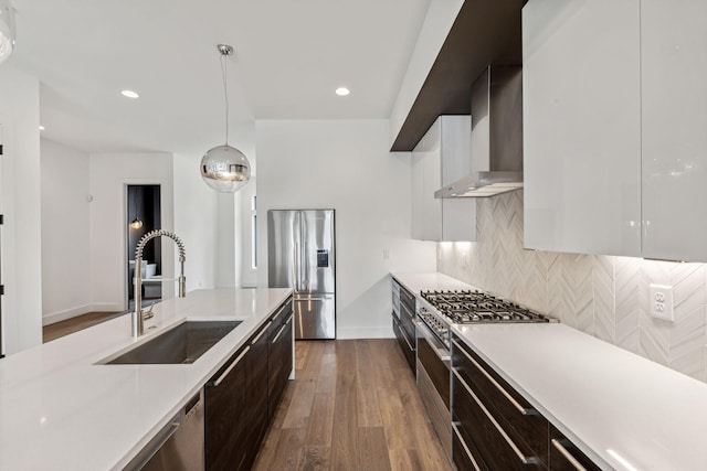 kitchen featuring appliances with stainless steel finishes, decorative light fixtures, white cabinetry, sink, and wall chimney exhaust hood