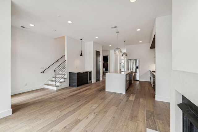 kitchen featuring stainless steel fridge, a kitchen island with sink, sink, and light hardwood / wood-style flooring