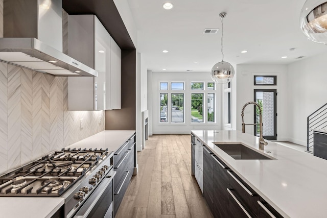 kitchen featuring tasteful backsplash, sink, hanging light fixtures, double oven range, and wall chimney range hood