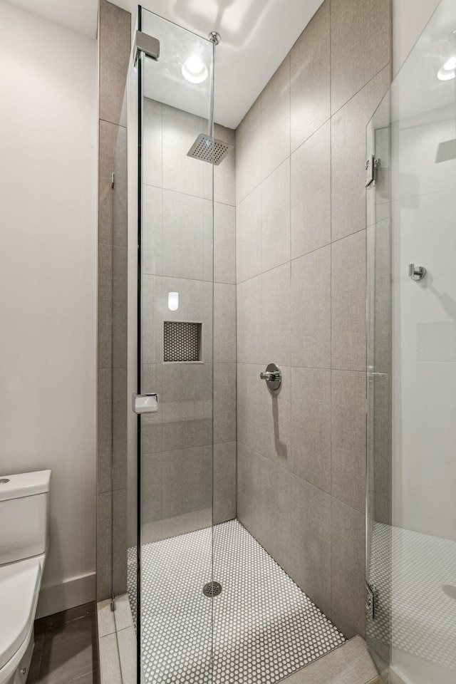 bathroom featuring a shower with door and toilet