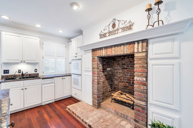 kitchen with sink, dark hardwood / wood-style floors, dark stone countertops, white cabinetry, and ornamental molding