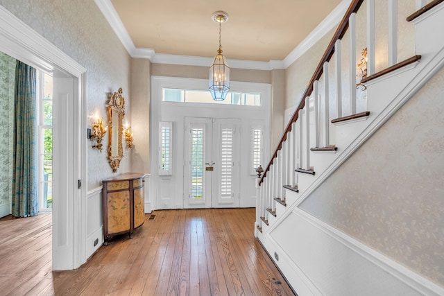 foyer featuring an inviting chandelier, hardwood / wood-style flooring, crown molding, and plenty of natural light