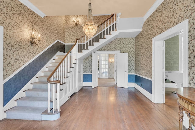 stairs featuring ornamental molding, an inviting chandelier, hardwood / wood-style floors, and a high ceiling