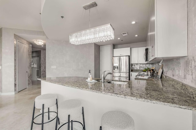 kitchen with white cabinetry, stainless steel appliances, kitchen peninsula, and light stone countertops